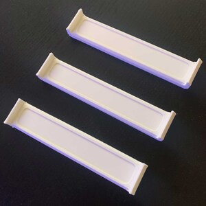 May include: Three white plastic shelf dividers, designed to help organize shelves in a kitchen, pantry, or bathroom.
