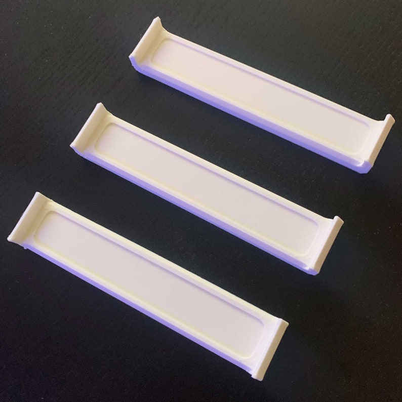 May include: Three white plastic shelf dividers, designed to help organize shelves in a kitchen, pantry, or bathroom.