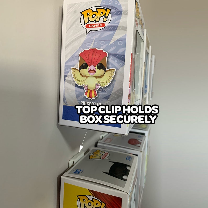 May include: A white wall mount display with a white clip holding a Pop! Games Pidgeotto figure in a box. The text "TOP CLIP HOLDS BOX SECURELY" is printed on the wall mount.