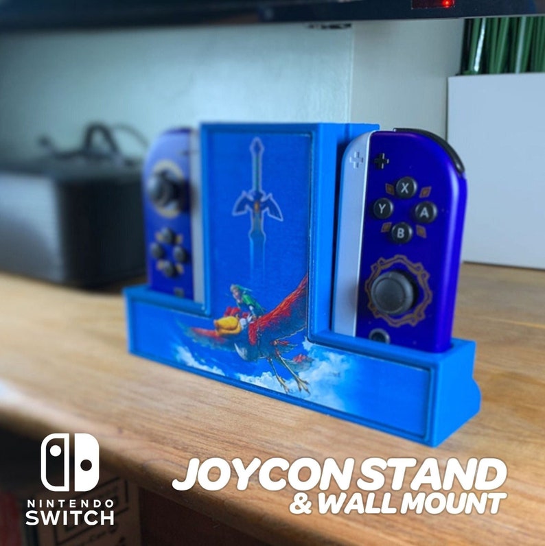 May include: A blue and white Nintendo Switch Joy-Con stand with a wall mount. The stand features a design from the Legend of Zelda: Breath of the Wild video game. The stand has a slot for each Joy-Con controller and a space for the Nintendo Switch console. The stand is made of 3D printed plastic.