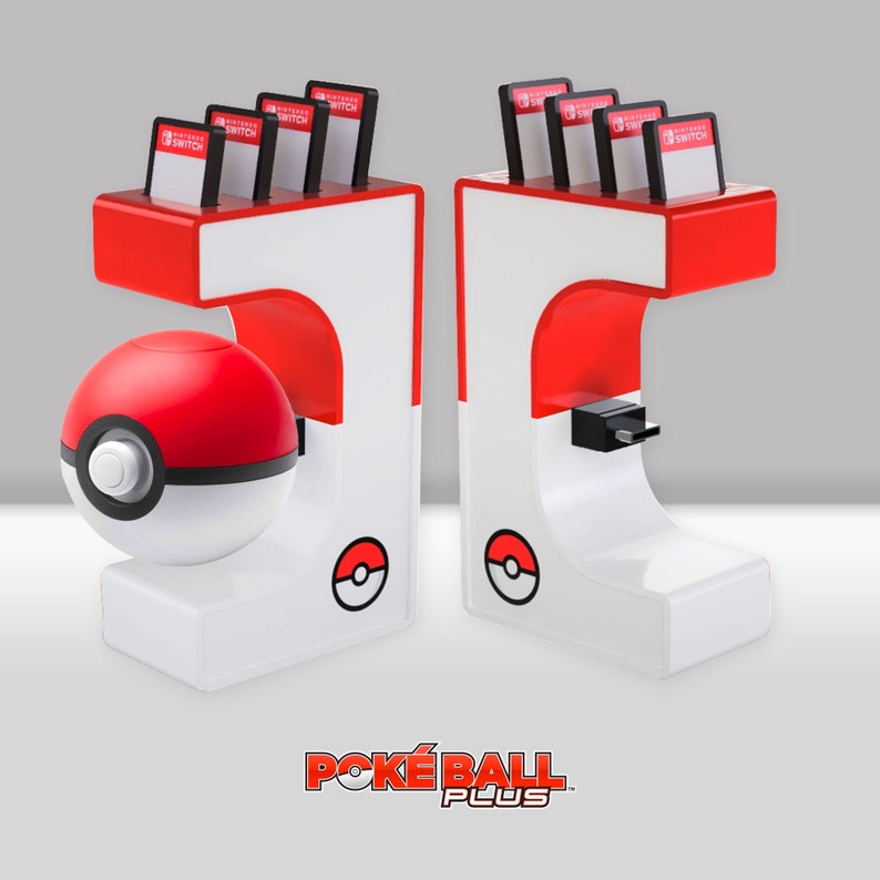 May include: A white and red Poke Ball Plus charging stand with two slots for Nintendo Switch game cartridges. The stand features a Poke Ball design with a red and white Poke Ball on the front. The stand is labeled "POKE BALL PLUS".