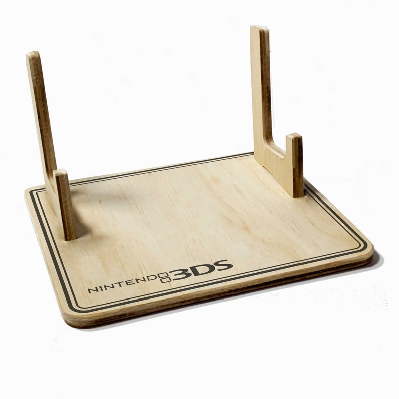 May include: A wooden Nintendo 3DS game console stand. The stand is rectangular with a light wood grain finish and a black border. The Nintendo 3DS logo is printed on the front.