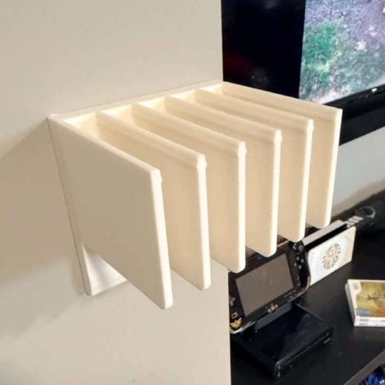 May include: A white wall-mounted shelf with six vertical slots. The shelf is made of a solid, opaque material and is designed to hold items. The shelf is mounted on a light gray wall.