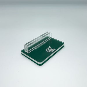 May include: A green acrylic stand with a clear acrylic insert. The stand has the words "GAME GEAR" printed on it.