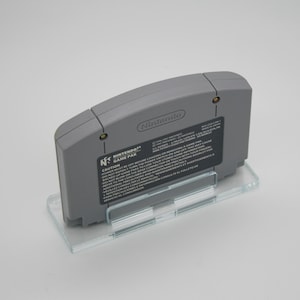 May include: A gray Nintendo 64 game cartridge with a white label that reads "Nintendo 64 Game Pak" and includes a warning about powering off the console before loading or removing a game pak. The label also includes instructions for handling the cartridge.
