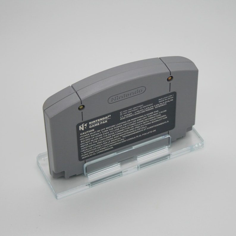 May include: A gray Nintendo 64 game cartridge with a white label that reads "Nintendo 64 Game Pak" and includes a warning about powering off the console before loading or removing a game pak. The label also includes instructions for handling the cartridge.