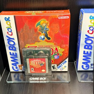 May include: A boxed copy of "The Legend of Zelda: Seasons" for Game Boy Color, featuring a red and orange design with game art. A clear cartridge with the game label is in front. The box reads "Nintendo" and "Only for Color."
