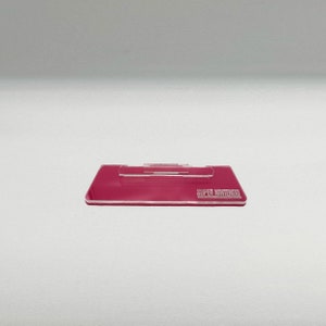 May include: A pink plastic stand for a Super Nintendo game cartridge. The stand has a slot for the cartridge and the words "SUPER NINTENDO" are printed on the front.