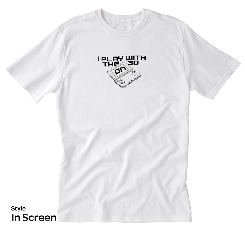 May include: White t-shirt with a black and white graphic of a Nintendo 3DS handheld gaming console. The graphic includes the text "I Play With The 3D".