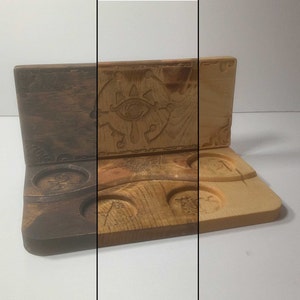 May include: A wooden box with a carved eye design on the lid. The box has five circular indentations on the bottom, likely for holding small items.