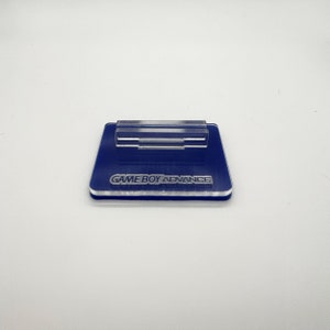 May include: A blue acrylic stand with a clear plastic holder for a Game Boy Advance cartridge. The stand has the words "GAME BOY ADVANCE" printed on it.