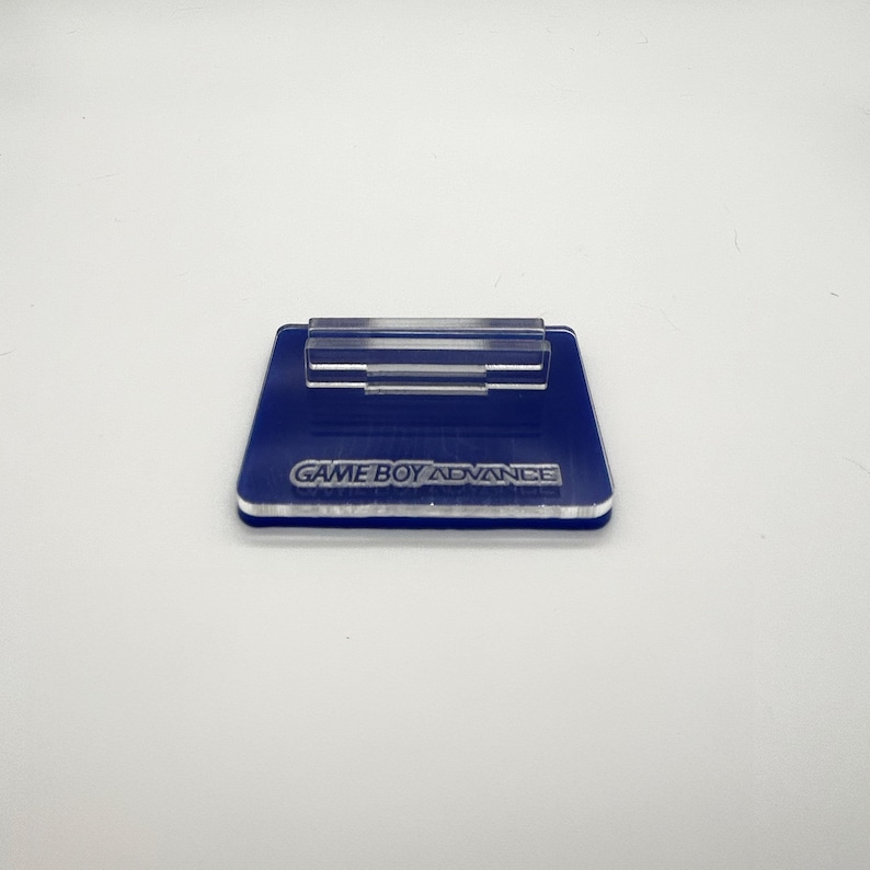 May include: A blue acrylic stand with a clear plastic holder for a Game Boy Advance cartridge. The stand has the words "GAME BOY ADVANCE" printed on it.
