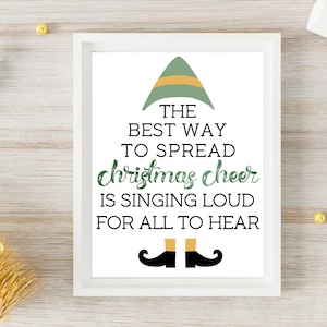 以下が含まれることがあります： 緑色のエルフの帽子と「THE BEST WAY TO SPREAD christmas cheer IS SINGING LOUD FOR ALL TO HEAR」というテキストが書かれた白い額縁付きのプリントです。