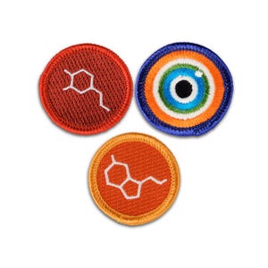 May include: Three circular embroidered patches. One is red with a white chemical structure, one is orange with a white chemical structure, and one features a concentric eye design in blue, orange, green, and white with a black pupil center.