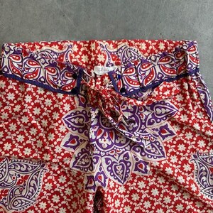 May include: Red and white patterned trousers with a purple and white floral design. The trousers have a drawstring waist and a decorative bow. The fabric is a soft, lightweight material, ideal for warmer weather.