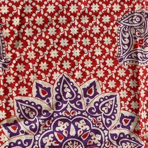 May include: Red fabric featuring a white floral pattern and large purple paisley and floral designs. The fabric has a repeating pattern of white star-shaped flowers on a red background.