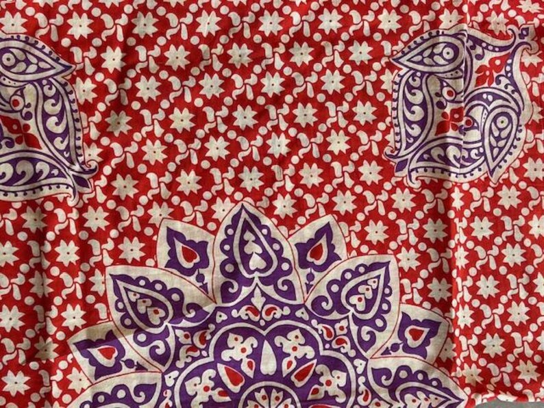 May include: Red fabric featuring a white floral pattern and large purple paisley and floral designs. The fabric has a repeating pattern of white star-shaped flowers on a red background.