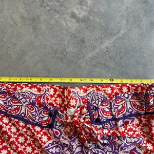 May include: Close-up of red and white patterned trousers with purple and blue trim. A yellow measuring tape is laid across the top, showing a measurement of approximately 33 cm.