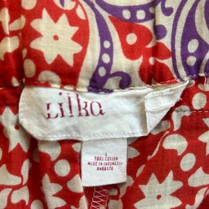 May include: Close-up of a fabric with a red and white floral pattern, and a purple and off-white paisley design. The tag reads "lilka" in red embroidery, with "100% cotton" and "Made in Indonesia" printed below.