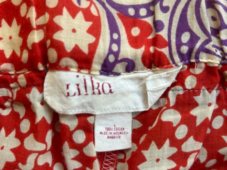 May include: Close-up of a fabric with a red and white floral pattern, and a purple and off-white paisley design. The tag reads "lilka" in red embroidery, with "100% cotton" and "Made in Indonesia" printed below.