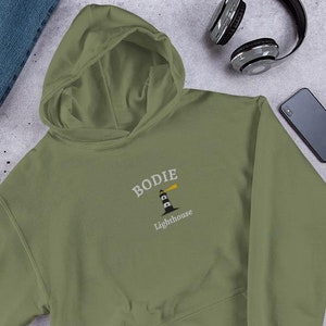 May include: A green hooded sweatshirt with the text "Bodie Lighthouse" embroidered on the front. The text is in white with a black and white illustration of a lighthouse.