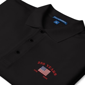 Close-up of embroidery on a black patriotic polo shirt for the USA 250th anniversary. Detailed stitching of the American flag and the years 1776 to 2026 in vibrant red thread. High-quality commemorative apparel for the American Semi quincentennial.
