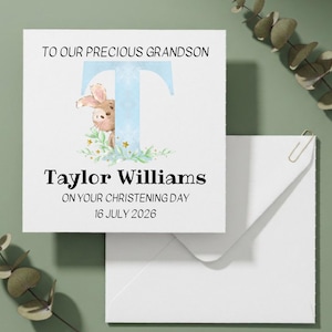 May include: A square white christening card featuring the text TO OUR PRECIOUS GRANDSON, a large light blue letter T, a small brown rabbit illustration, green foliage, gold stars, and the name Taylor Williams with 16 JULY 2026.