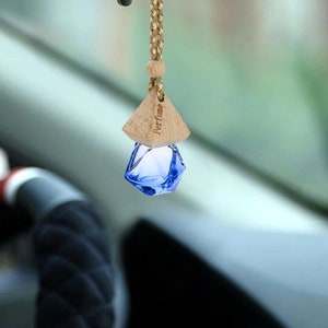 May include: A hanging car air freshener bottle featuring a faceted, translucent blue glass container suspended by a braided cord. The bottle is topped with a light-colored wooden cap that has the word Perfume engraved on its side surface.