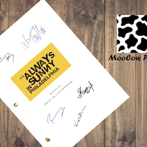 May include: A white script featuring the title "It's Always Sunny in Philadelphia" in black and yellow, with signatures in blue and black ink. The script is held together with brass fasteners. A MooCow Prints logo is in the upper right corner.