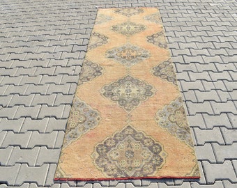 Op de afbeelding: Een vintage loper met een traditioneel Perzisch ontwerp in tinten oranje, beige en grijs. De loper heeft een vervaagde, verweerde uitstraling en is perfect om een ​​bohemien touch aan elke kamer toe te voegen.