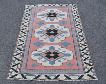 May include: A vintage rug with a pink background and a white, blue, and black geometric pattern. The rug has a fringed edge.