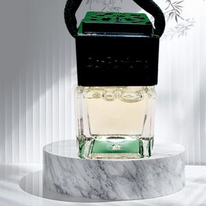 May include: A clear glass bottle with a black and green lid, hanging from a black string. The bottle is filled with a light yellow liquid and is sitting on a white marble surface.