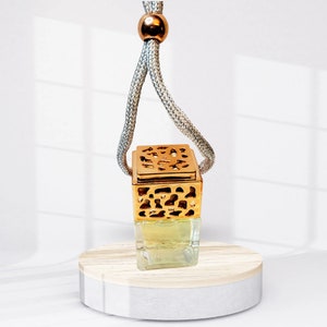 May include: A gold and clear glass car air freshener with a decorative metal cage. The air freshener is hanging from a gray string with a gold bead at the top.