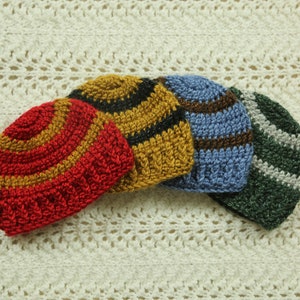 Peut inclure: Quatre bonnets en crochet de différentes couleurs et motifs. Les bonnets sont rouge et or, jaune et noir, bleu et marron, et vert et blanc.