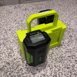 May include: A black and green 40V lithium battery pack with a charge indicator light, positioned in front of a bright lime green plastic storage mount featuring the Ryobi brand name embossed on the top handle for tool organization.
