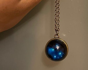 May include: A gold chain necklace with a round pendant featuring a blue galaxy with stars.