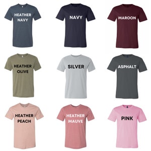 May include: Nine different solid-color t-shirts are displayed. Colors include heather navy, navy, maroon, heather olive, silver, asphalt, heather peach, heather mauve, and pink. Each shirt has the color name printed in white.