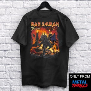 May include: Black t-shirt featuring a graphic of a dark figure with a crown against a red background. The text "Iron Sauron The Lord" is printed in yellow on the shirt.