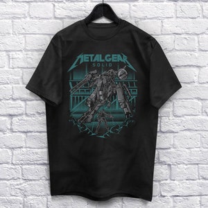 Puede incluir: Camiseta negra con un gráfico de un Metal Gear Solid mech en un esquema de color turquesa. El texto "METAL GEAR SOLID" está por encima del mech.