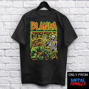 Puede incluir: Camiseta negra con un gráfico verde y amarillo de un personaje llamado Blanka de la serie de videojuegos Street Fighter. El gráfico muestra a Blanka luchando contra un esqueleto. El texto "Blanka" está escrito en letras amarillas sobre el gráfico. El texto "ONLY FROM METAL THRILLS" está escrito en letras blancas sobre un fondo azul en la esquina inferior derecha de la imagen.