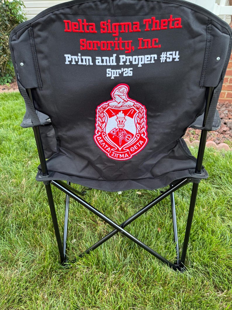 May include: Black folding chair with the text "Delta Sigma Theta Sorority, Inc. Prim and Proper #54 Spr'26" in red and white. The chair has a red and white emblem on the back.