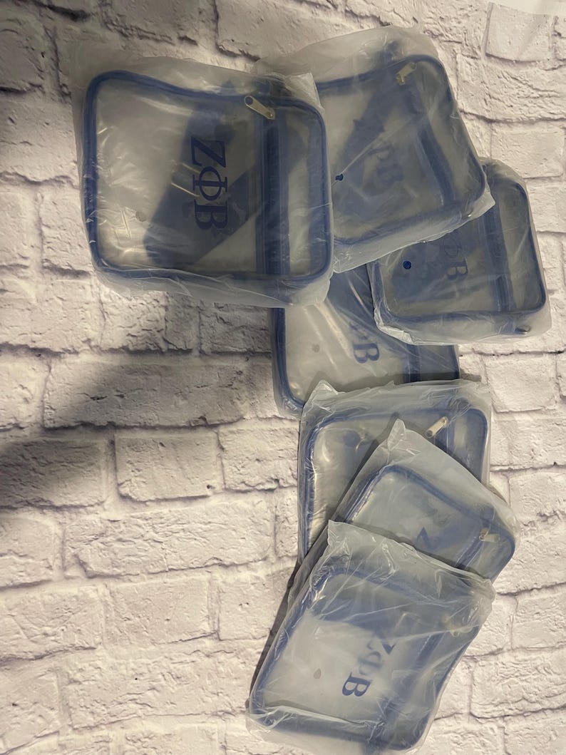 Puede incluir: Varias bolsas de pl&aacute;stico transparentes con ribetes azules, cada una contiene una bolsa de bandolera de pl&aacute;stico transparente con una cremallera azul y las letras "ZOB" impresas en azul en la parte delantera.