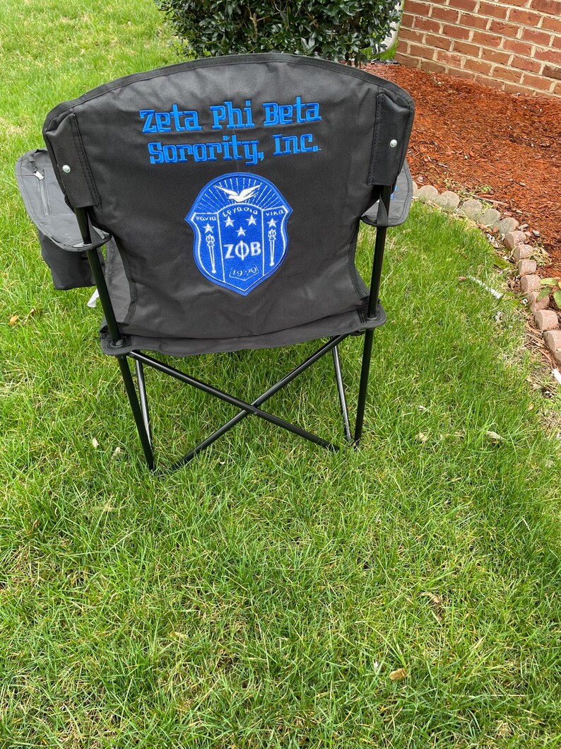 May include: Black folding outdoor chair with the text "Zeta Phi Beta Sorority, Inc." in blue. The chair back features a blue and white emblem with the letters "ZFB" and the founding year, 1920.