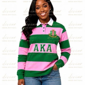Peut inclure: Un maillot de rugby à manches longues avec des rayures horizontales roses et vertes, un col blanc et une patte de boutonnage. Le maillot affiche les lettres AKA en vert sur la poitrine et un écusson sur le côté gauche, porté avec un jean bleu.
