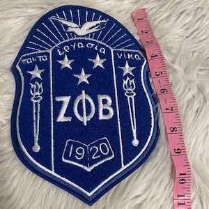 May include: A blue and white embroidered patch with the letters "ZOB" and the year "1920" in white. The patch features a white dove, three white stars, and two white torches.