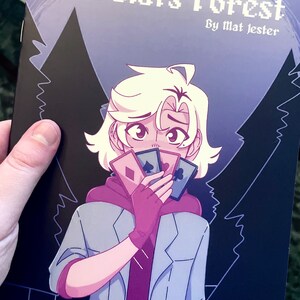 May include: A comic book cover with a purple and black background featuring a character with white hair holding playing cards in front of their face. The title of the comic is "Lorelai's Forest" by "Mat Jester".