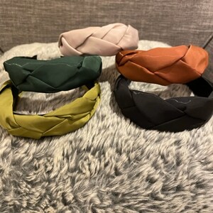 May include: Five braided headbands in different colors: green, pink, brown, black, and olive green. The headbands are made of a soft, stretchy fabric and are designed to be comfortable to wear.