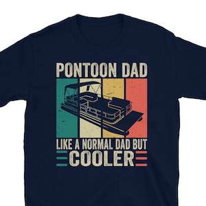 May include: Navy blue t-shirt with a retro graphic design. The design features a pontoon boat illustration with the text "PONTOON DAD LIKE A NORMAL DAD BUT COOLER" in a vintage style. The shirt is made of a soft material.