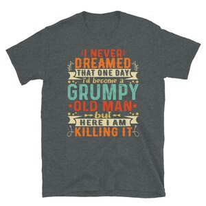 May include: A dark heather grey t-shirt with a vintage-style graphic that reads "I never dreamed that one day I'd become a grumpy old man, but here I am killing it".