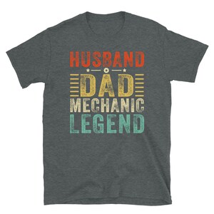 May include: A dark heather grey t-shirt with a vintage-style graphic that reads "Husband Dad Mechanic Legend".